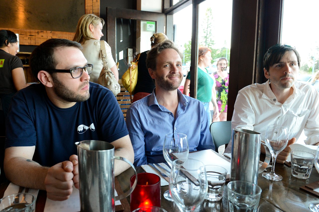Three men sit at a restaurant table with glasses and pitchers, engaged in conversation during DrupalCon Sydney 2013.