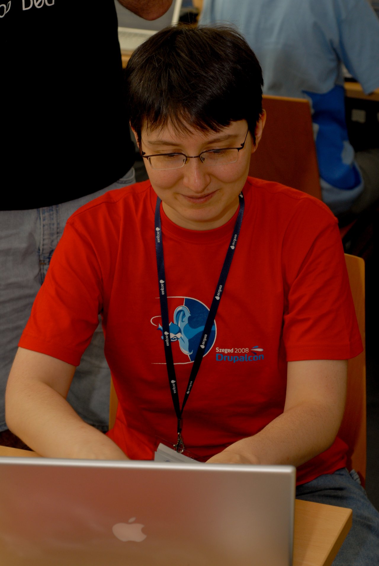 A person wearing a red DrupalCon 2008 shirt is working on a laptop at a conference.