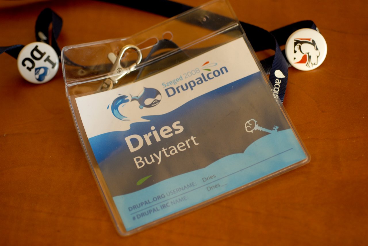 A DrupalCon Szeged 2008 conference badge with a name tag inside, attached to a lanyard with buttons.