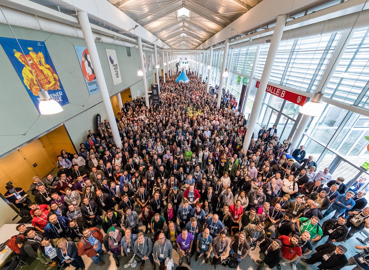 A large group of people gathered indoors for a group photo at DrupalCon Vienna 2017, looking at the camera.