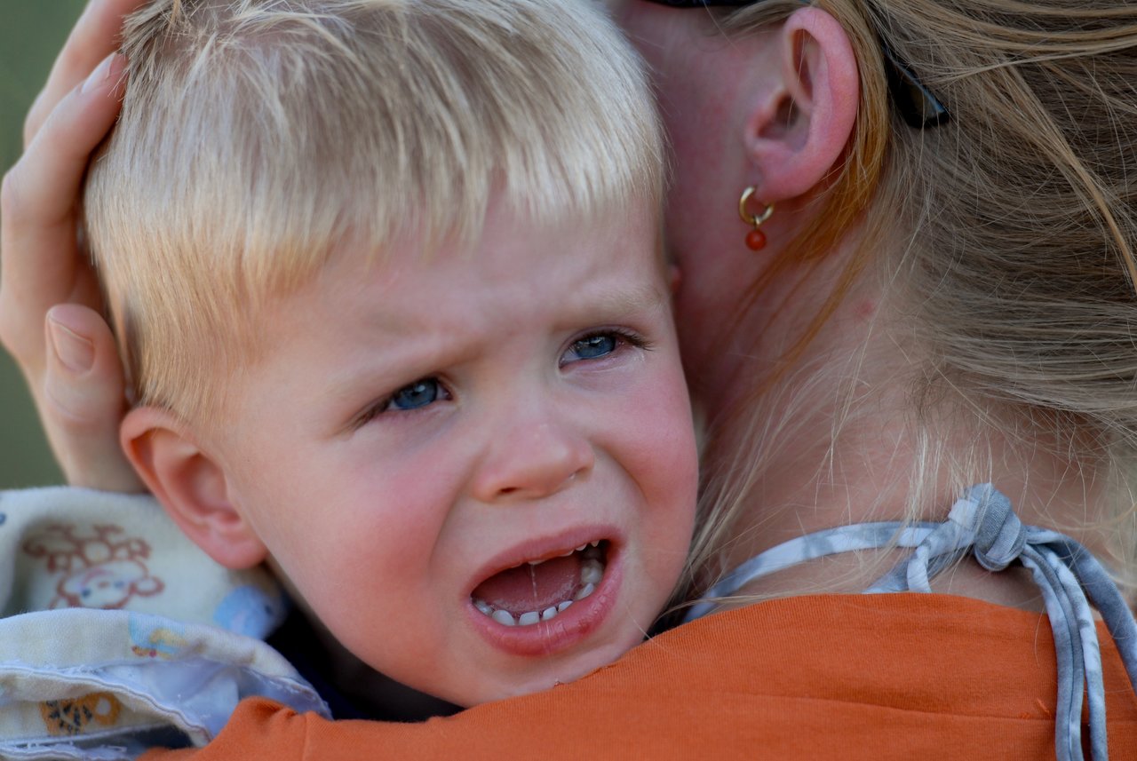 A crying young child is held closely by an adult, who is comforting them with a gentle embrace.
