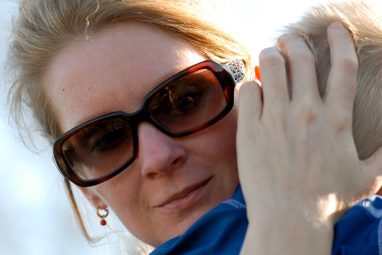 A woman wearing sunglasses holds a child close, gently resting her hand on the child's head.