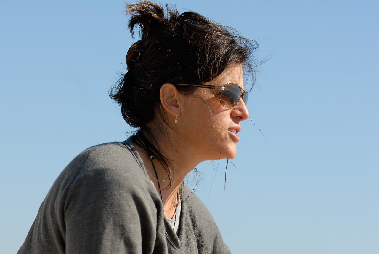 A woman wearing sunglasses and a gray sweater looks to the side with a focused expression.