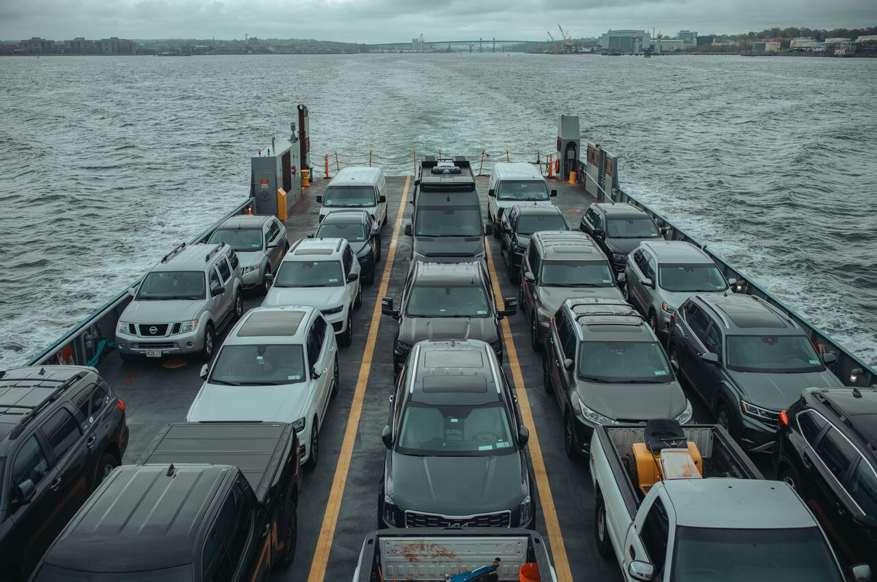 View from the back of a ferry packed with cars and vans crossing open water.