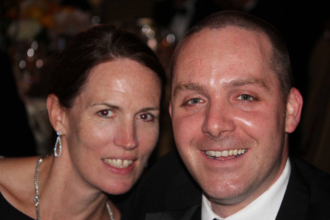 A smiling man and woman pose closely together at an award banquet.