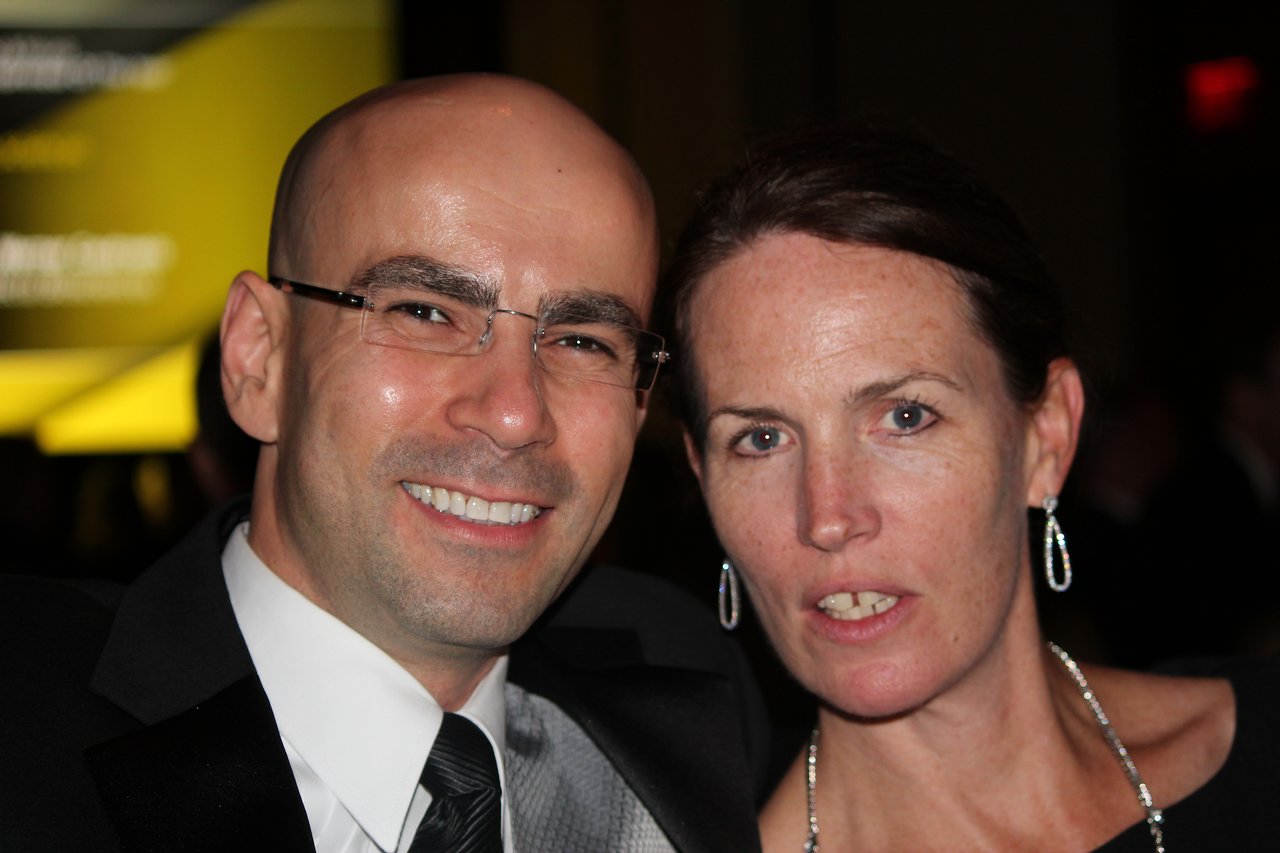 A man and woman dressed in formal attire pose together at an award banquet, smiling at the camera.