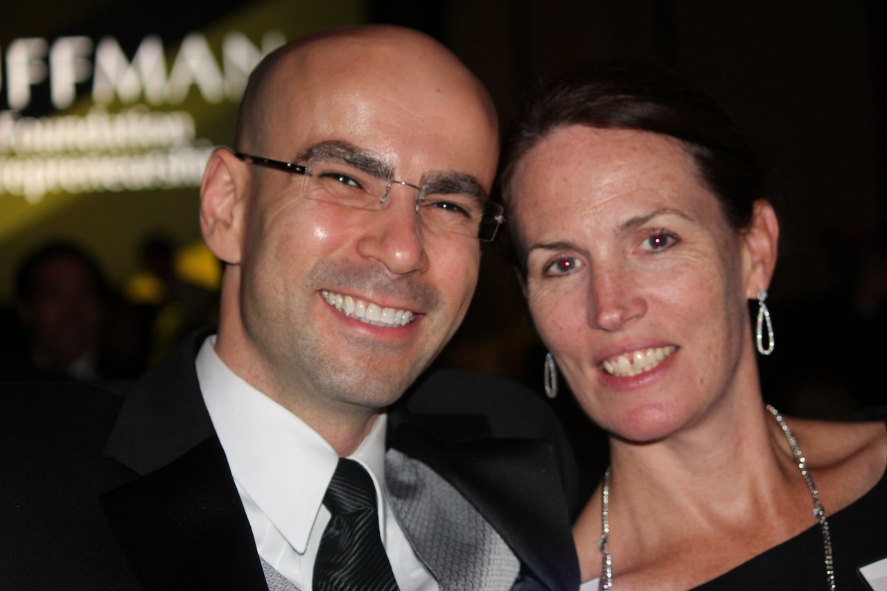 A smiling man and woman pose together at an award banquet, dressed in formal attire.