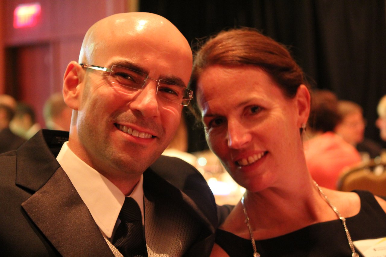 A man and woman smile while seated at a formal award banquet, dressed in elegant attire.