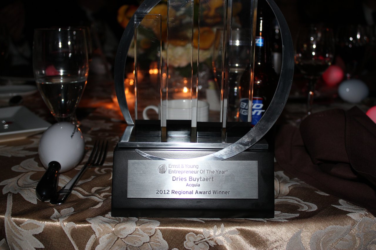A close-up of an Ernst &amp; Young award trophy on a banquet table with glasses and decorations in the background.