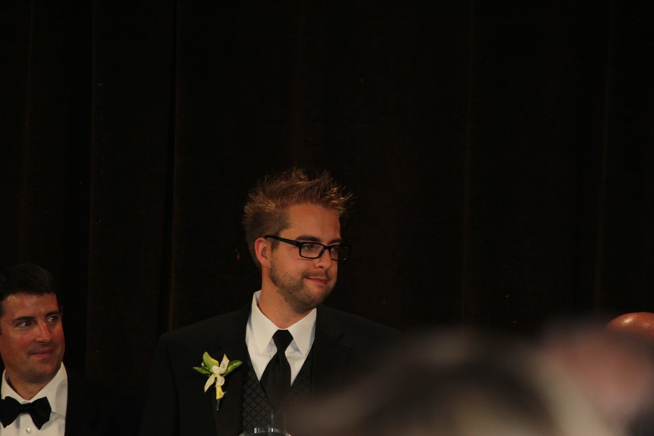 A man in a suit with a boutonniere stands at an award banquet, looking to the side.