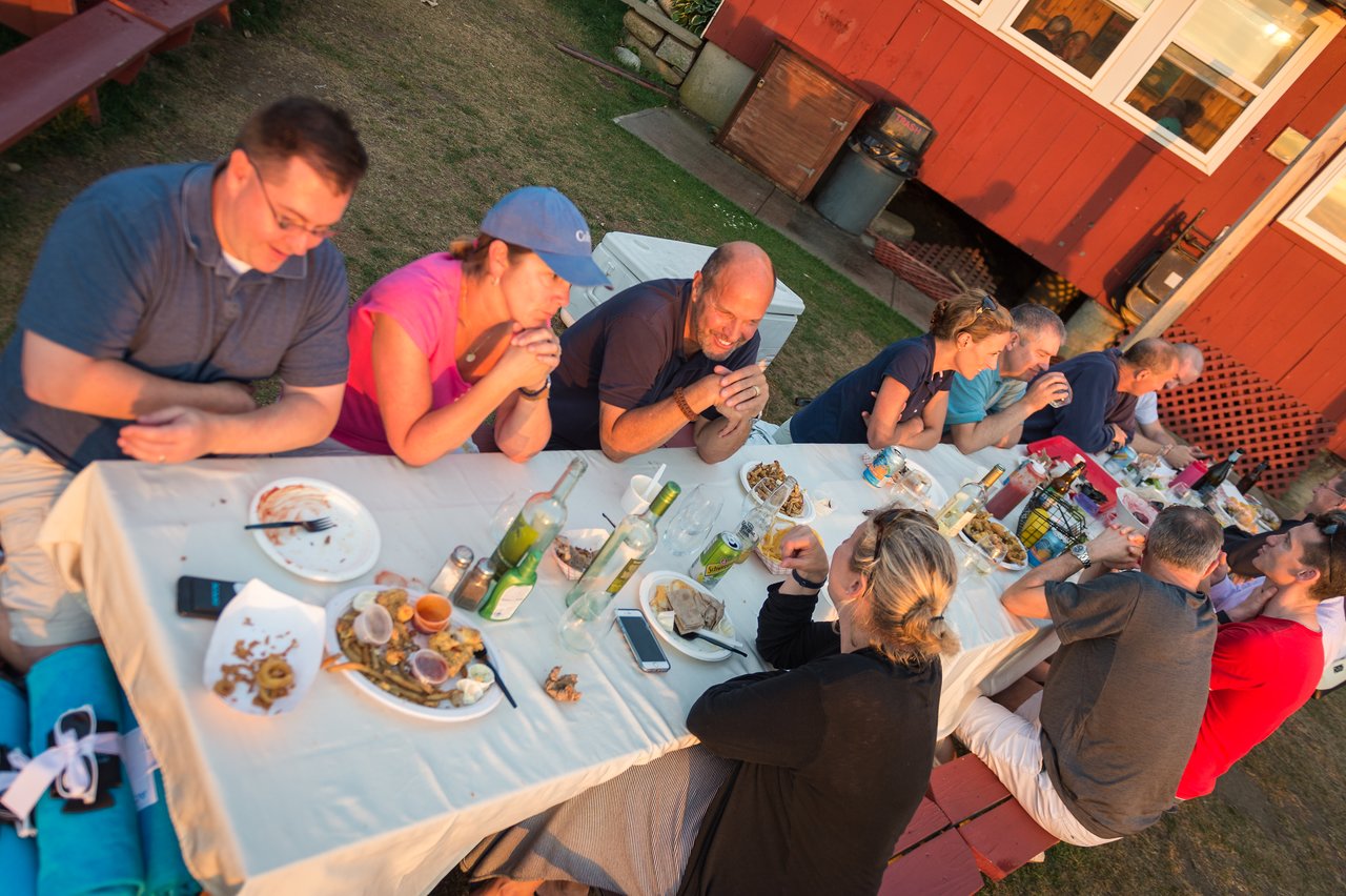 A group of people gathered at an outdoor table, eating lobster and other food during a dinner event.