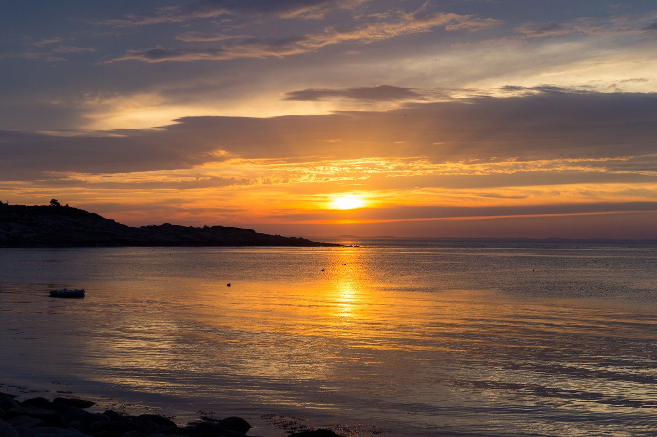 A calm coastal scene at sunset with the sun reflecting on the water.