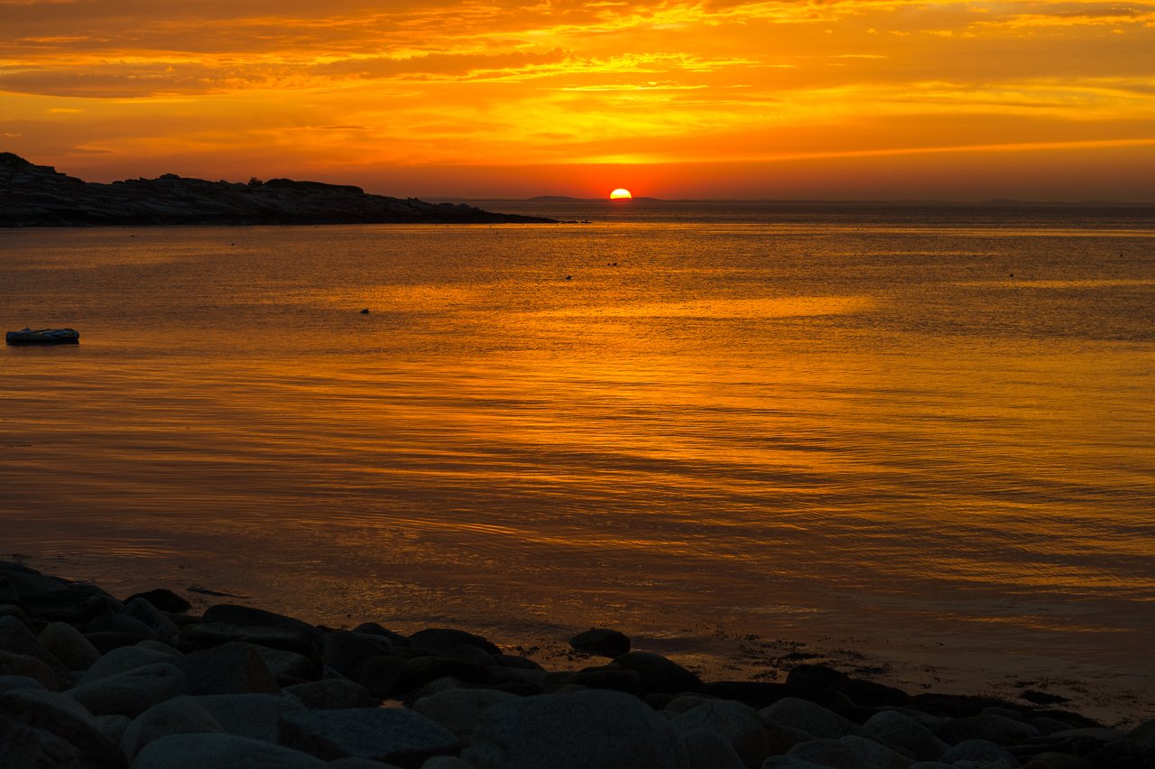 A sunset over the ocean with rocky shoreline in the foreground.