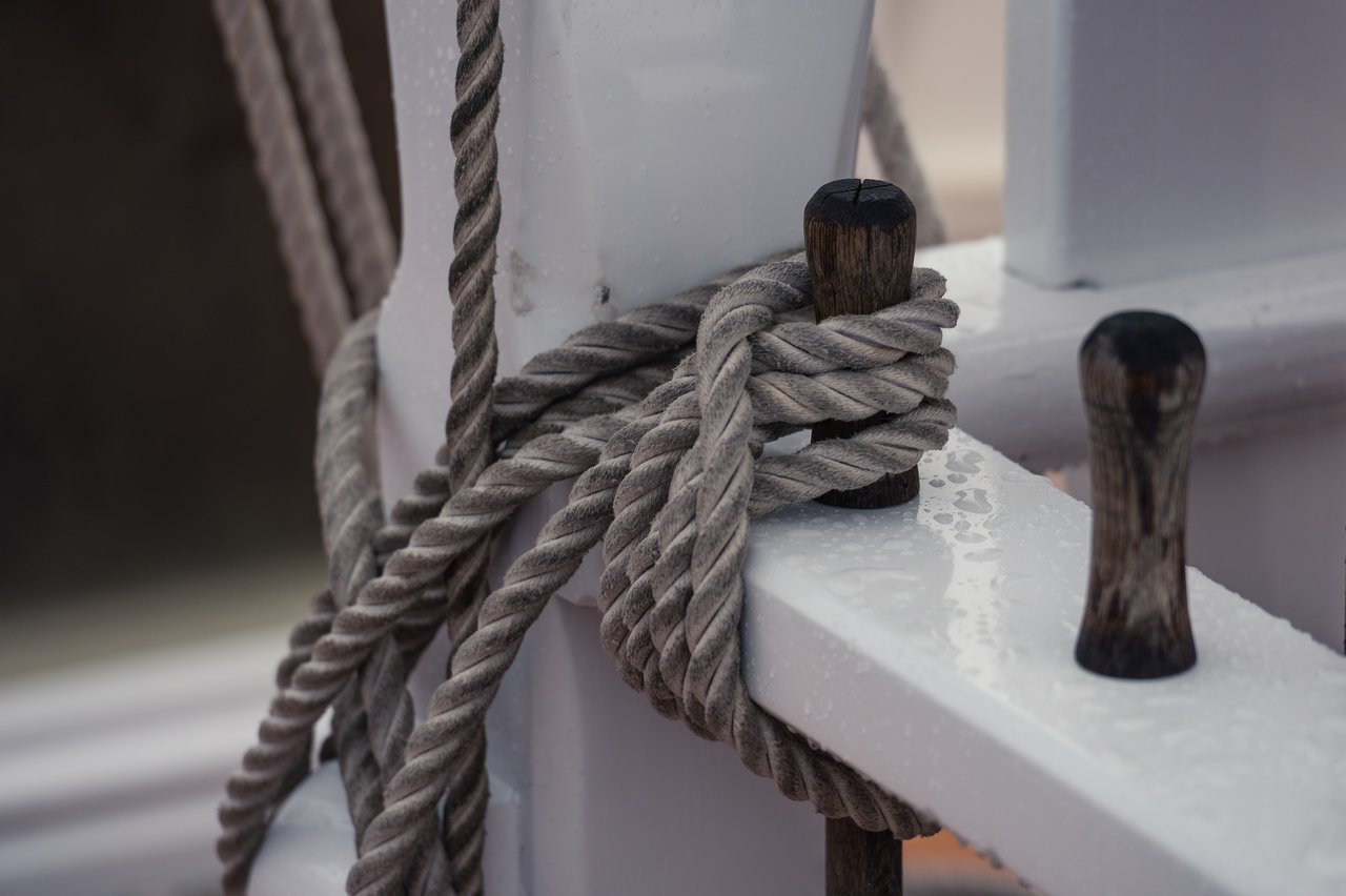 Close-up of a thick rope tightly wrapped around wooden pegs on a wet sailing boat.