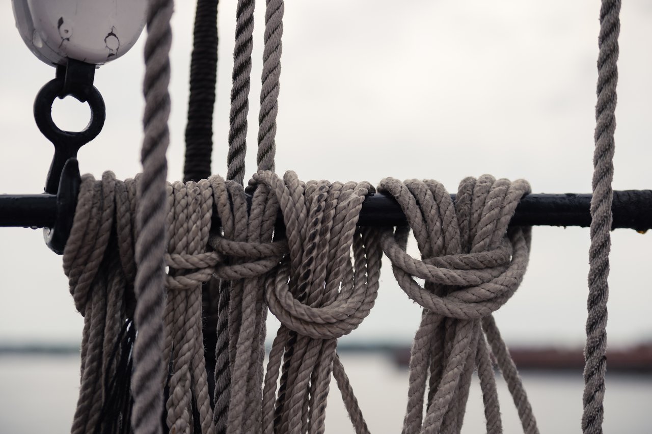 Close-up of neatly coiled sailing ropes secured to a metal bar on a boat, with water in the background.
