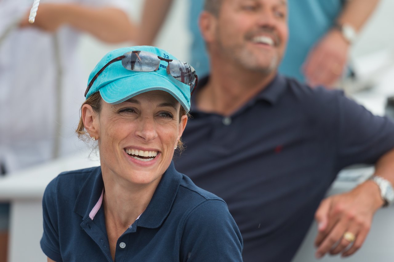 A woman in a blue cap smiles while sailing, with others in the background enjoying the experience.
