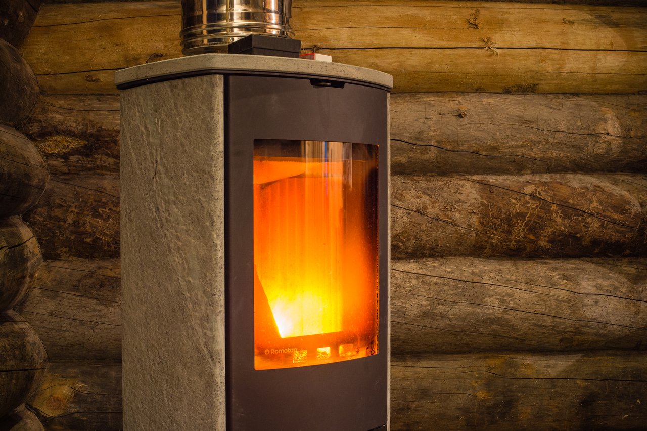 A wood-burning fireplace with a glass door showing a bright fire inside, set against a log cabin wall.
