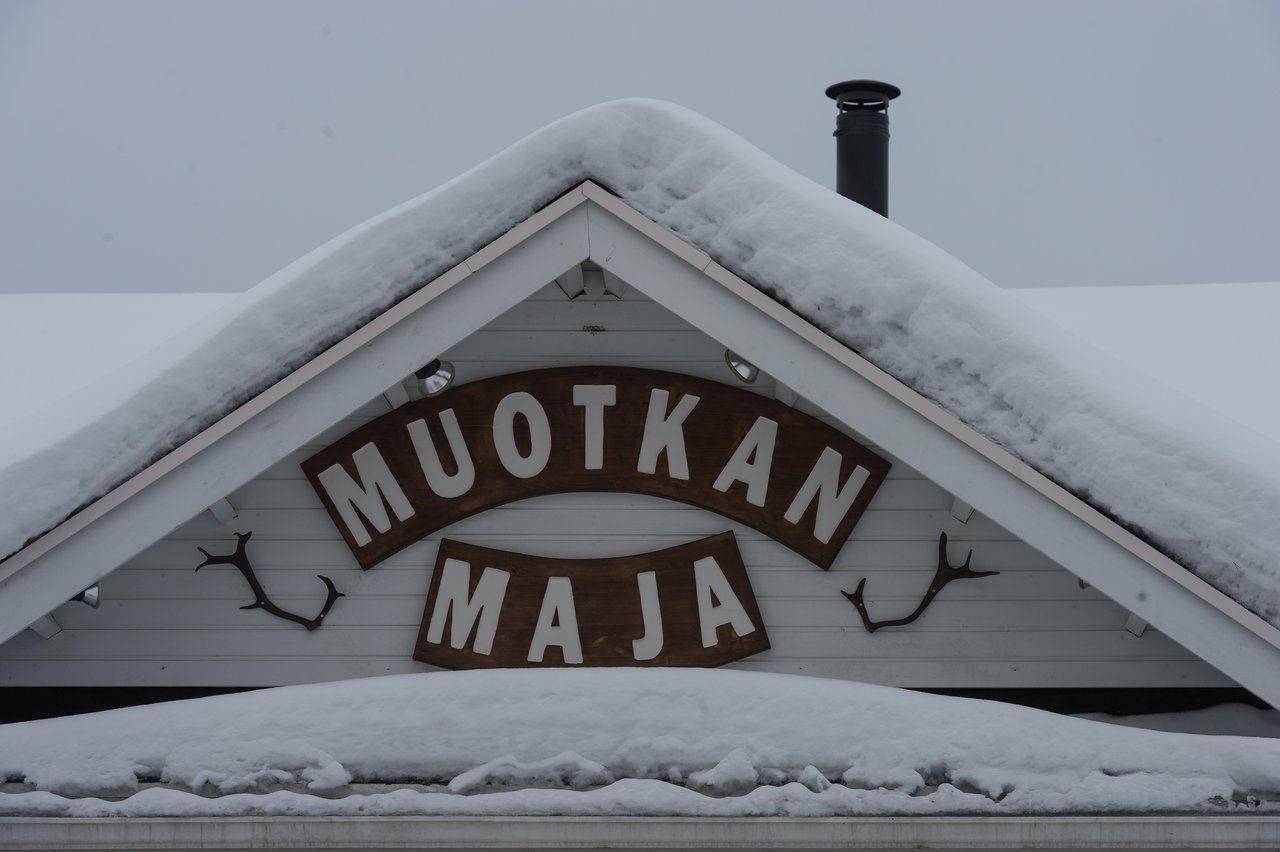 Snow-covered roof of Muotkan Maja wilderness hotel with a wooden sign and decorative antlers on the wall.