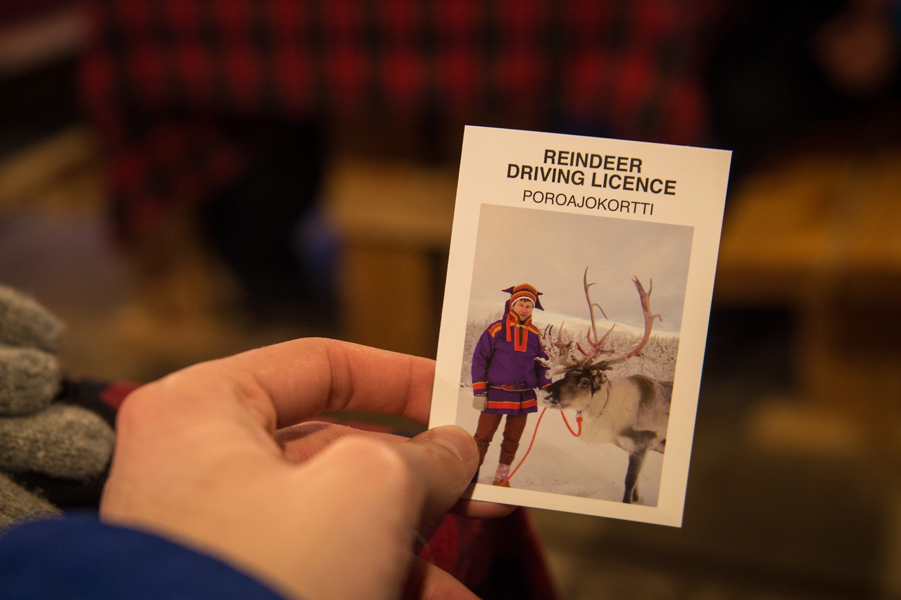 A person holds a "Reindeer Driving Licence" card featuring an image of a man with a reindeer in the snow.