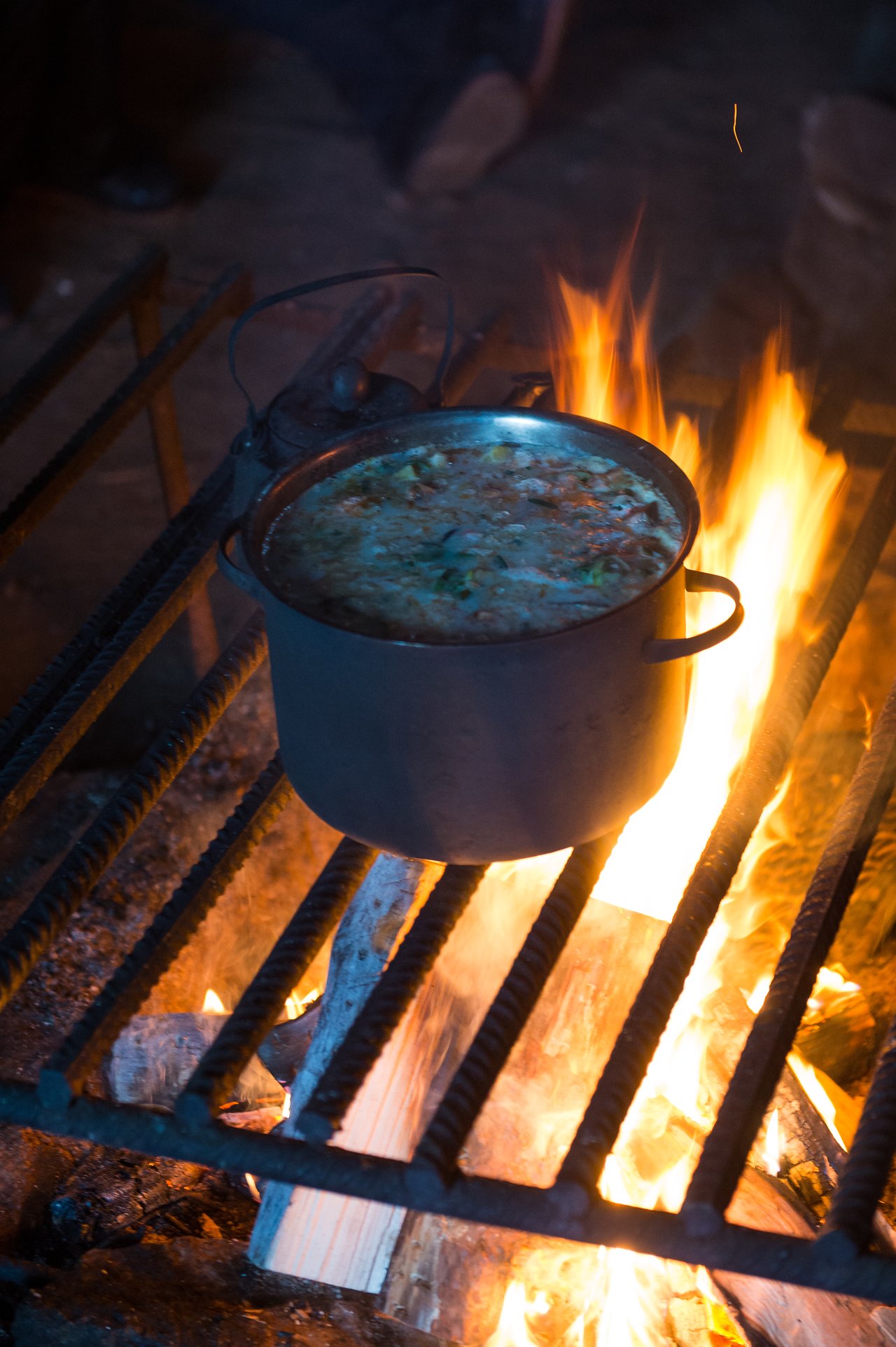 A pot of salmon soup cooking over an open fire on a metal grate.