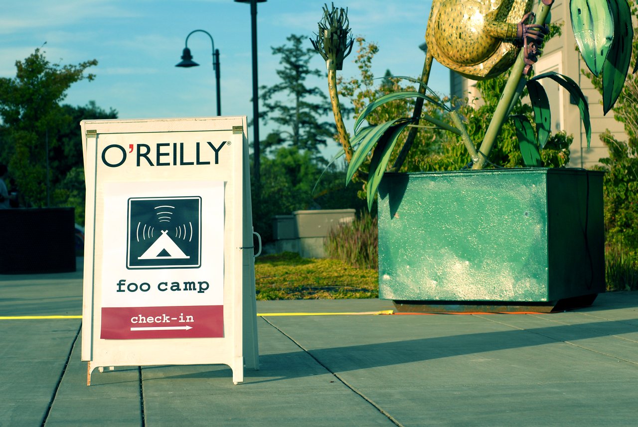 A sign for Foo Camp check-in stands on a sidewalk, directing attendees to the registration area.