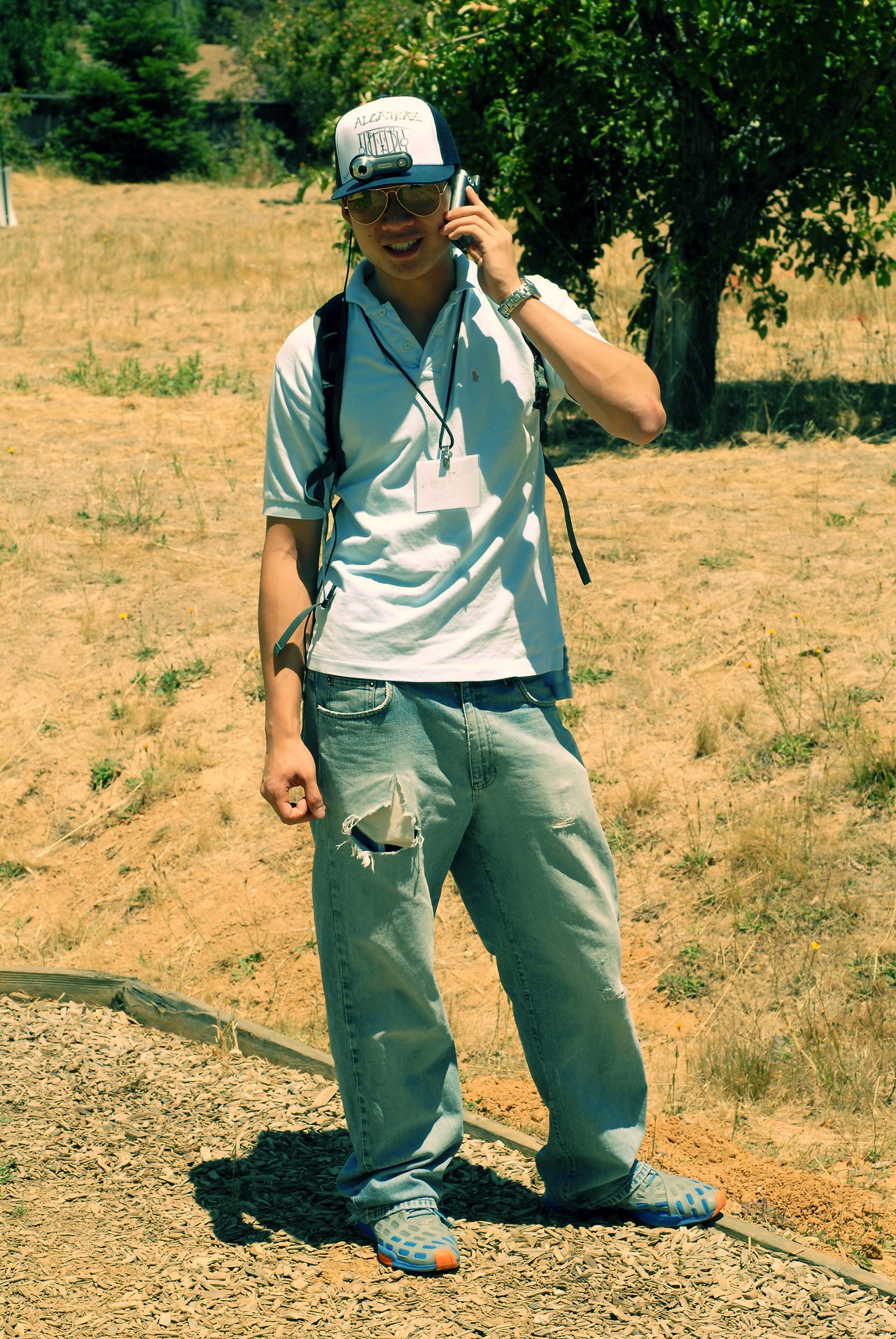 A man wearing a cap-mounted camera walks outdoors while talking on his phone, streaming his life online in real-time.