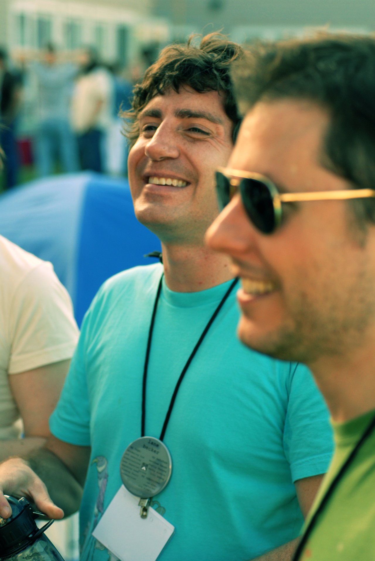 Two men smiling and talking at an outdoor event, one wearing sunglasses and the other wearing a name badge.