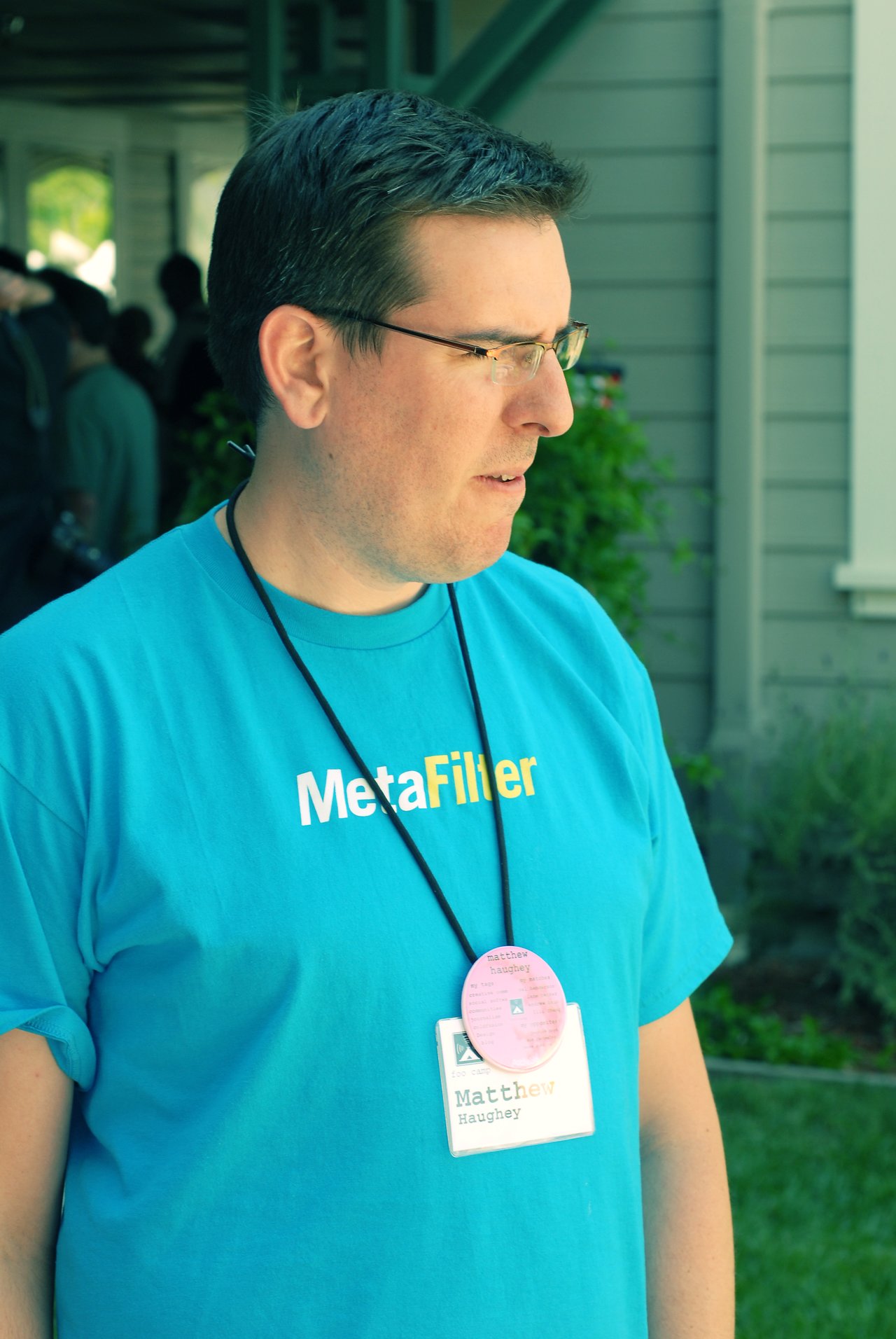 A man wearing a blue "MetaFilter" shirt and name badge stands outside, looking to the side.