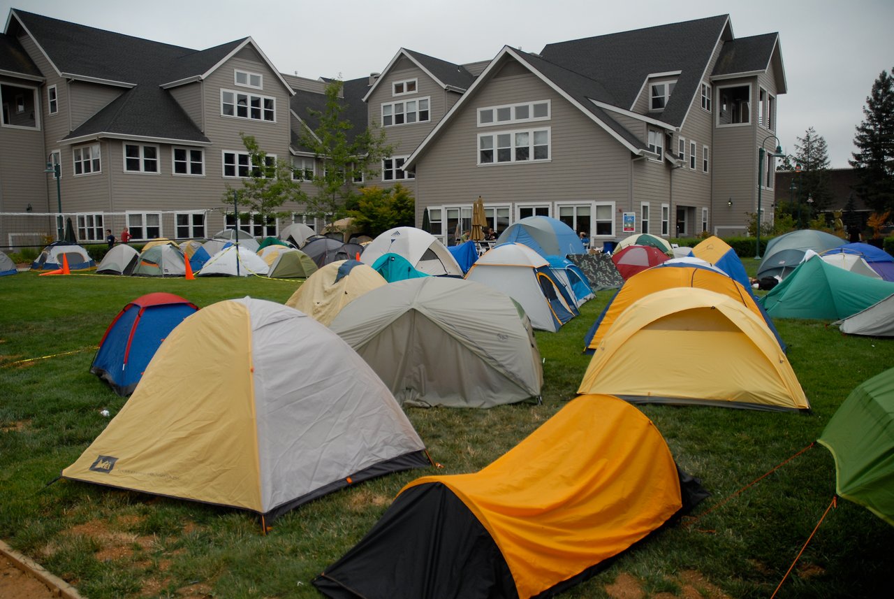 A large number of tents are set up on a grassy field outside a multi-story building during an event.