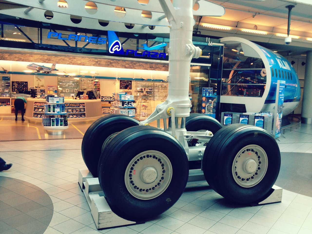 Large airplane landing gear display in an airport terminal, with a store selling aviation-related items in the background.
