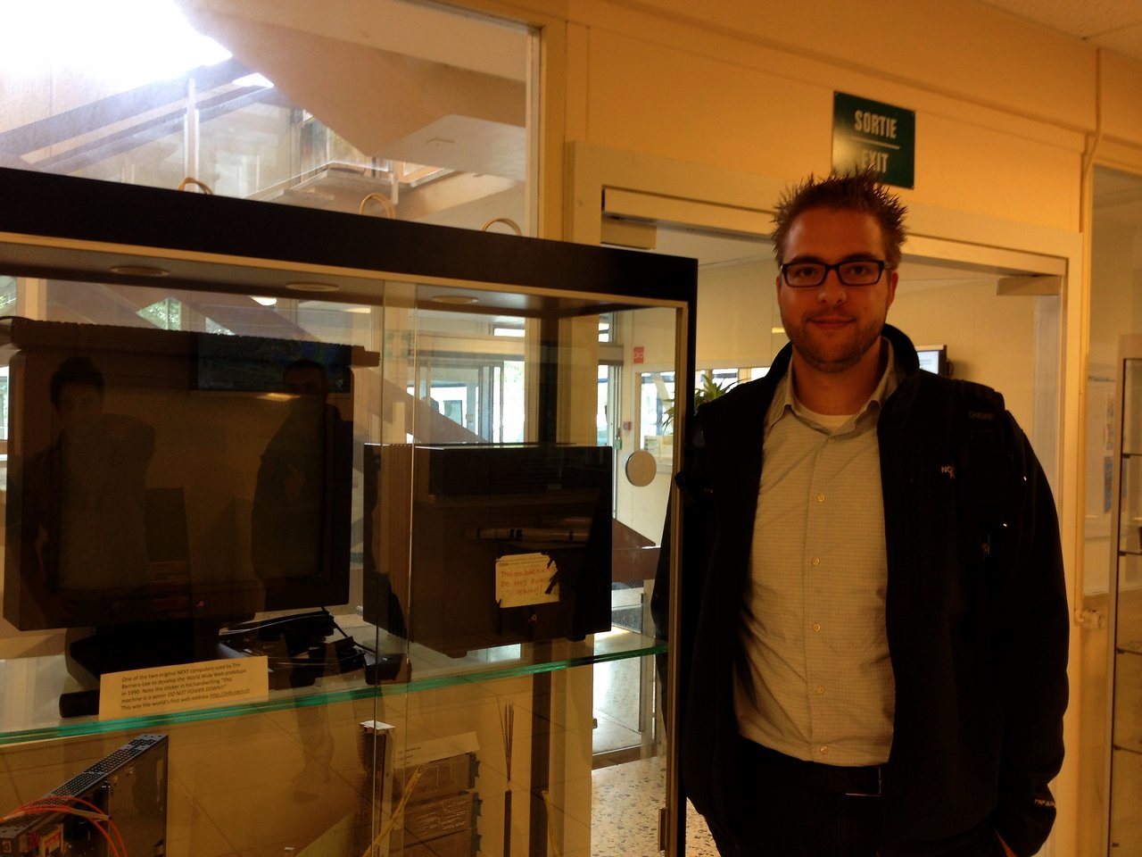 A man stands next to a glass case displaying the first web server ever used at CERN.