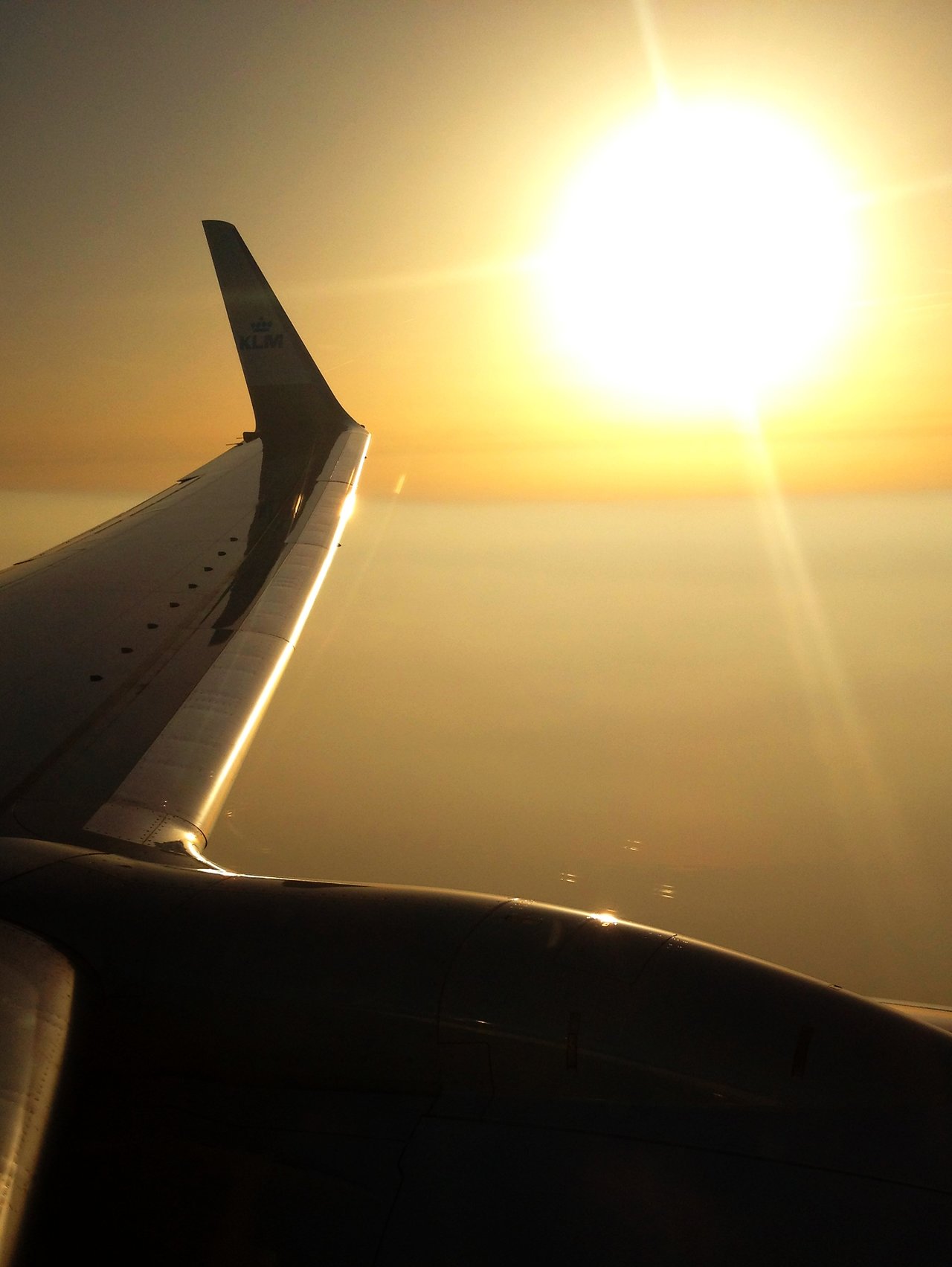 View from an airplane window showing the wing and engine, with the sun shining brightly in the sky.
