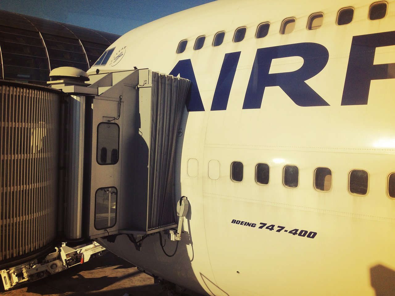A jet bridge is connected to the upper deck door of an Air France Boeing 747-400 at the airport.