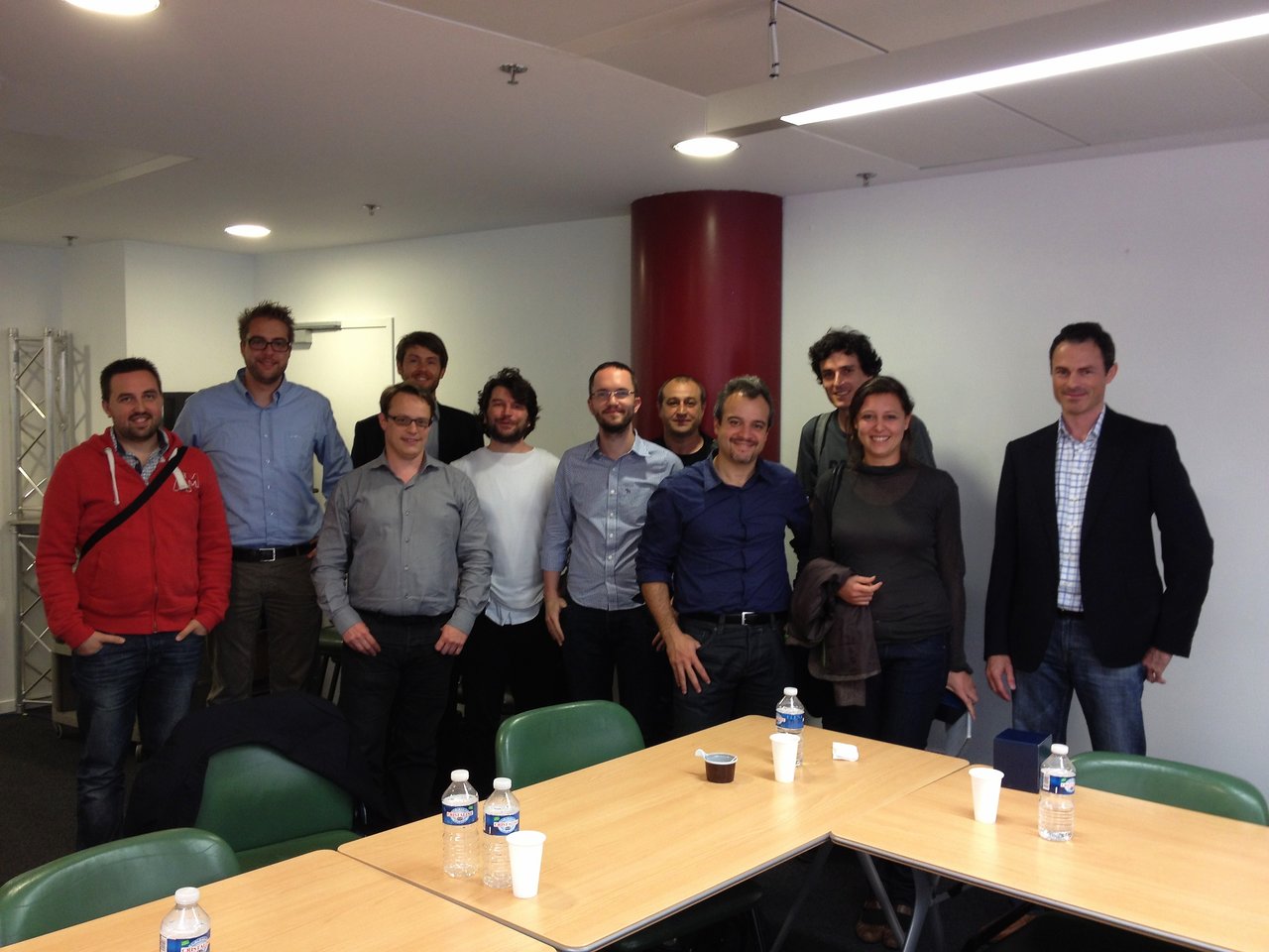 A group of people posing in a meeting room, likely media professionals from French organizations, standing near tables with water bottles.