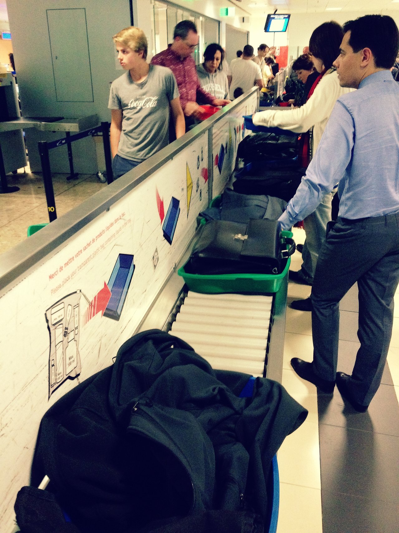 Passengers at Geneva Airport place their belongings in trays for security screening at a checkpoint conveyor belt.