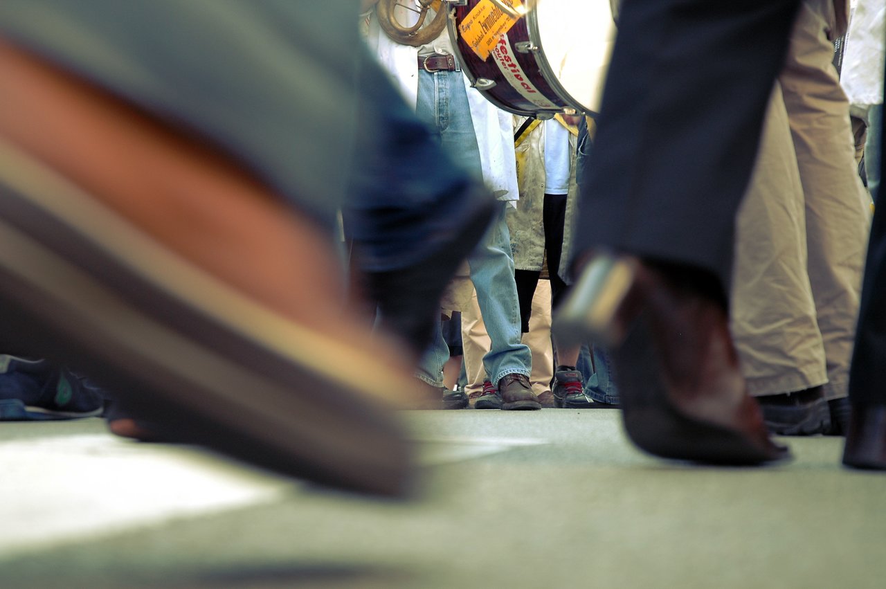 People marching on a street, with moving feet in the foreground and a drummer visible in the background.