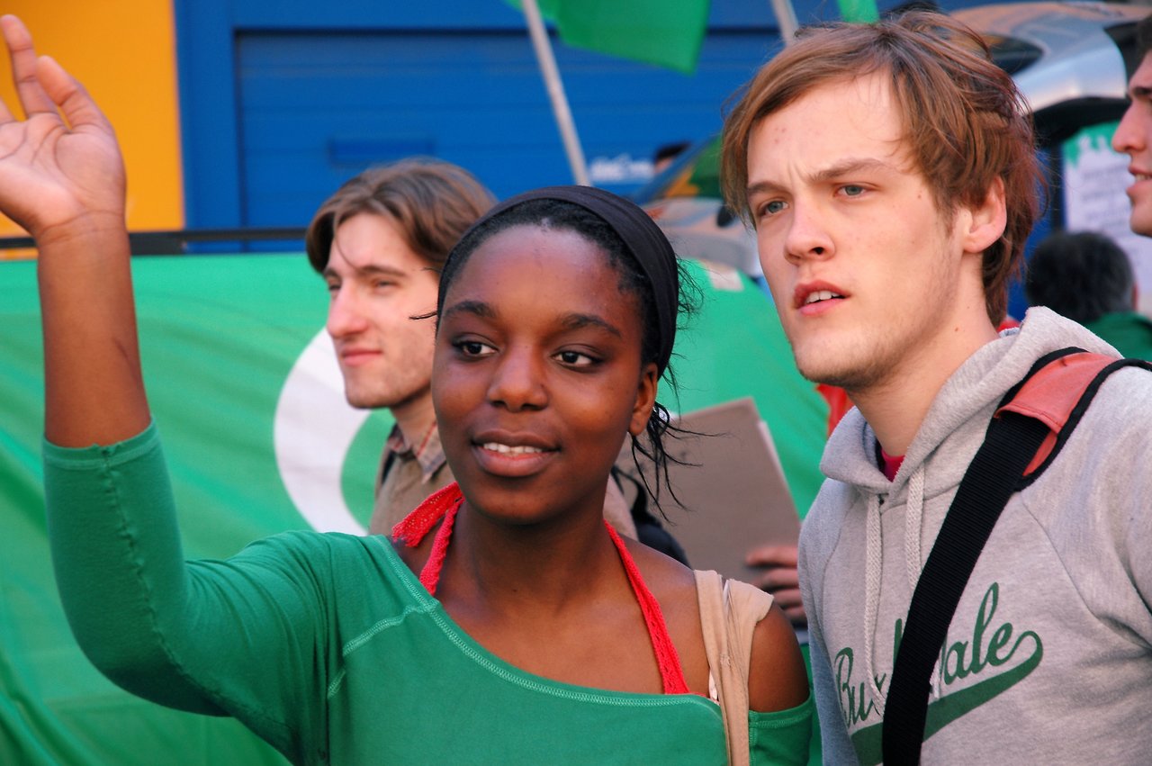 A group of protesters participates in a demonstration, with one person raising their hand and others holding signs.
