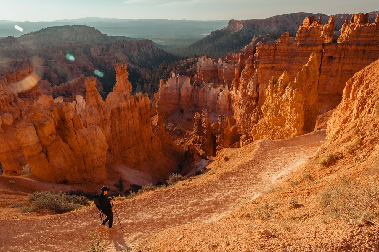 A woman with trekking poles hiking down a switchback trail among tall orange hoodoos in Bryce Canyon National Park.