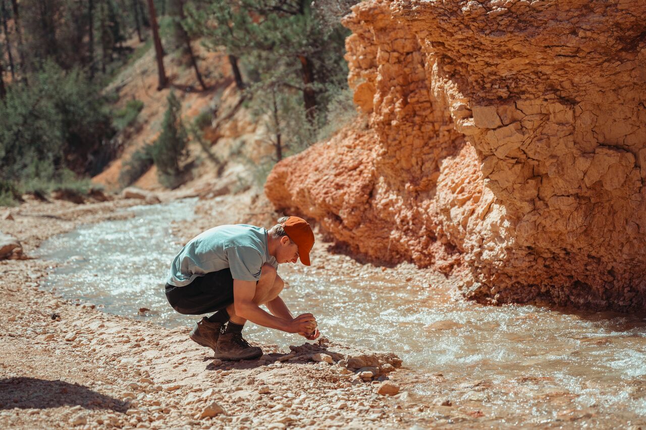 Young man crouching by a stream in Bryce Canyon, trying to crack open rocks in the water.