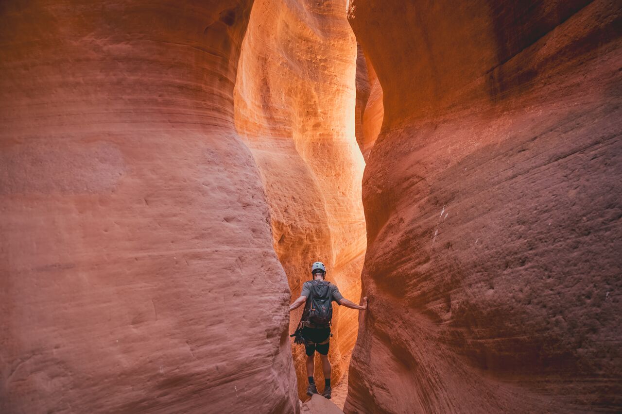 A person carefully walking along a narrow sandstone slot canyon in Zion National Park.