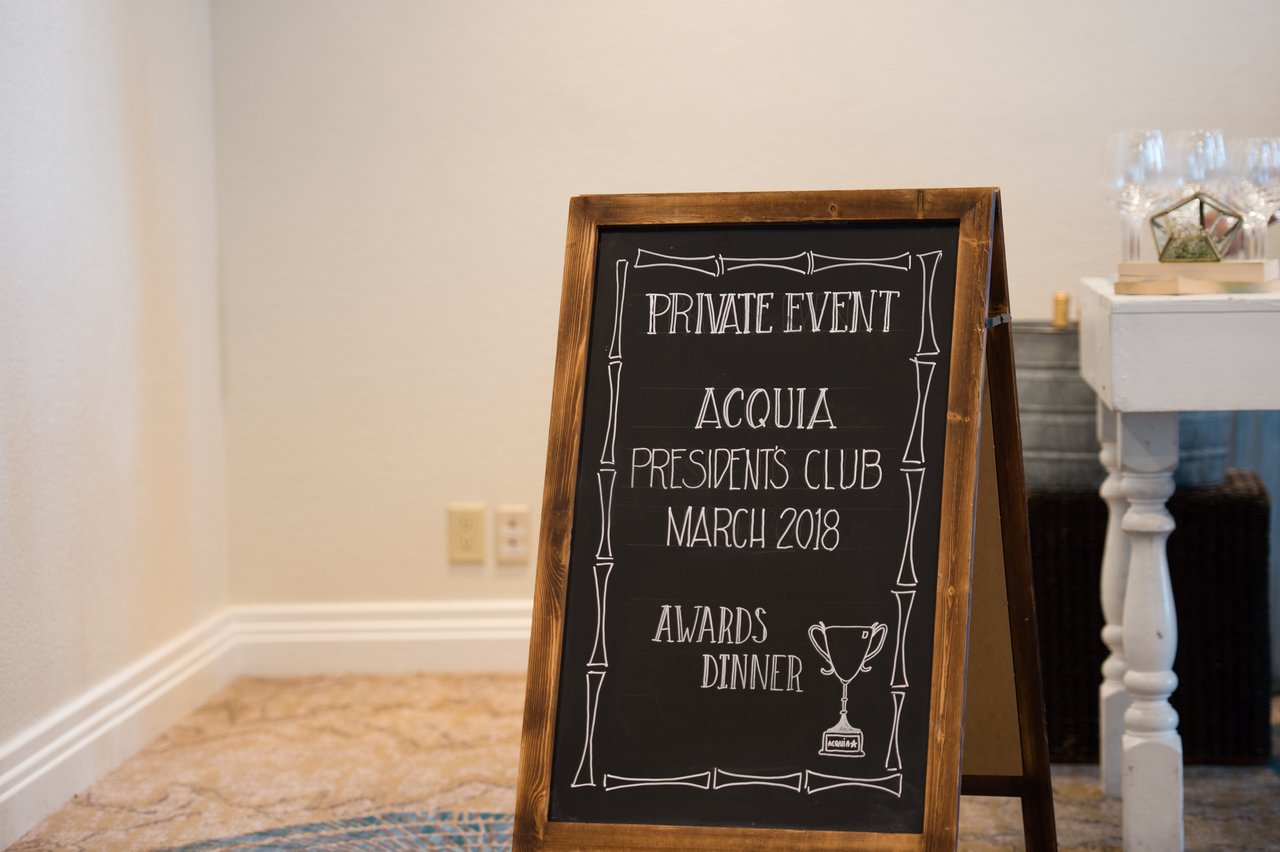 A chalkboard sign announces the Acquia President's Club Awards Dinner, a private event in March 2018.