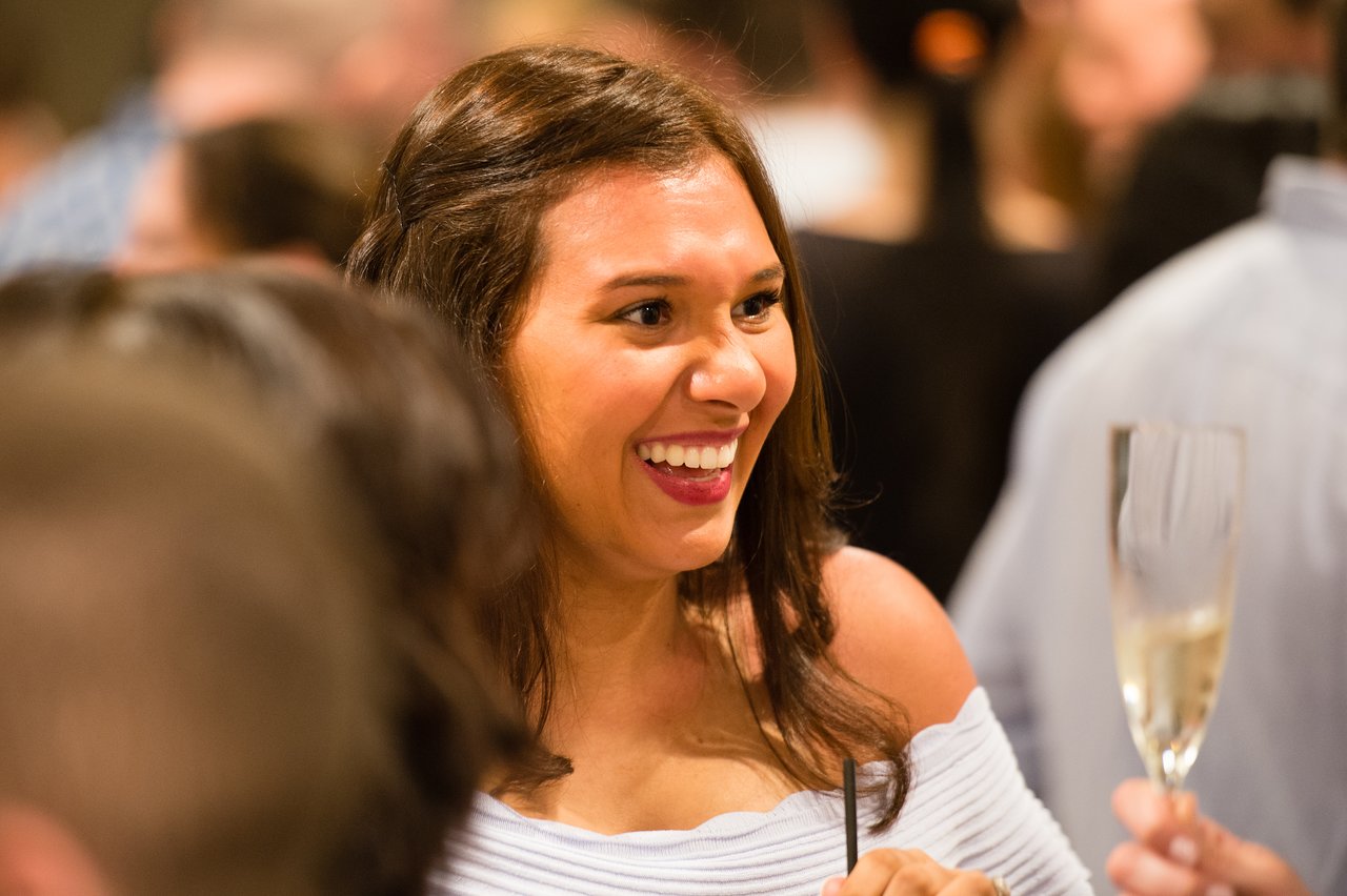 A woman smiles while holding a drink at an awards dinner during a company trip.