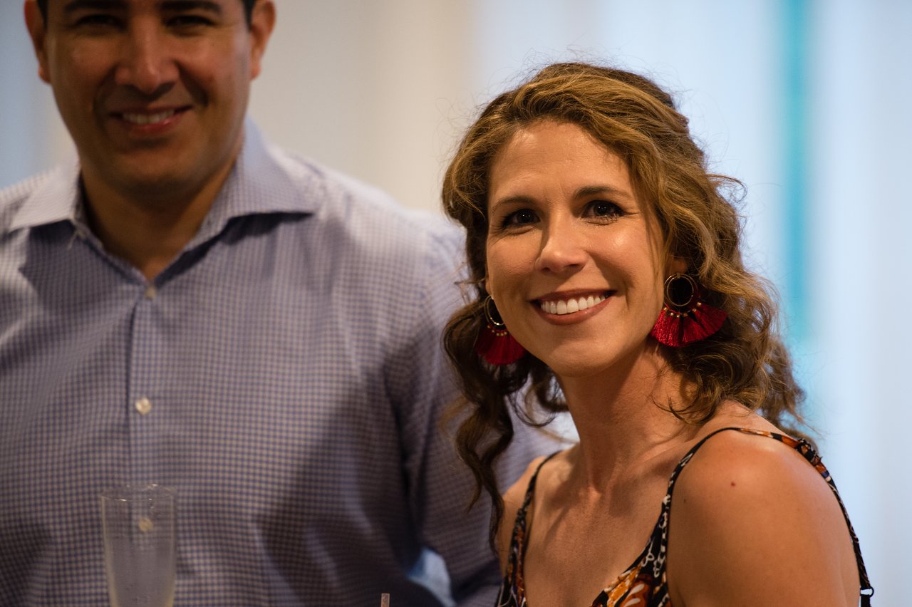 A woman smiles at the camera during an awards dinner, with a man standing beside her.