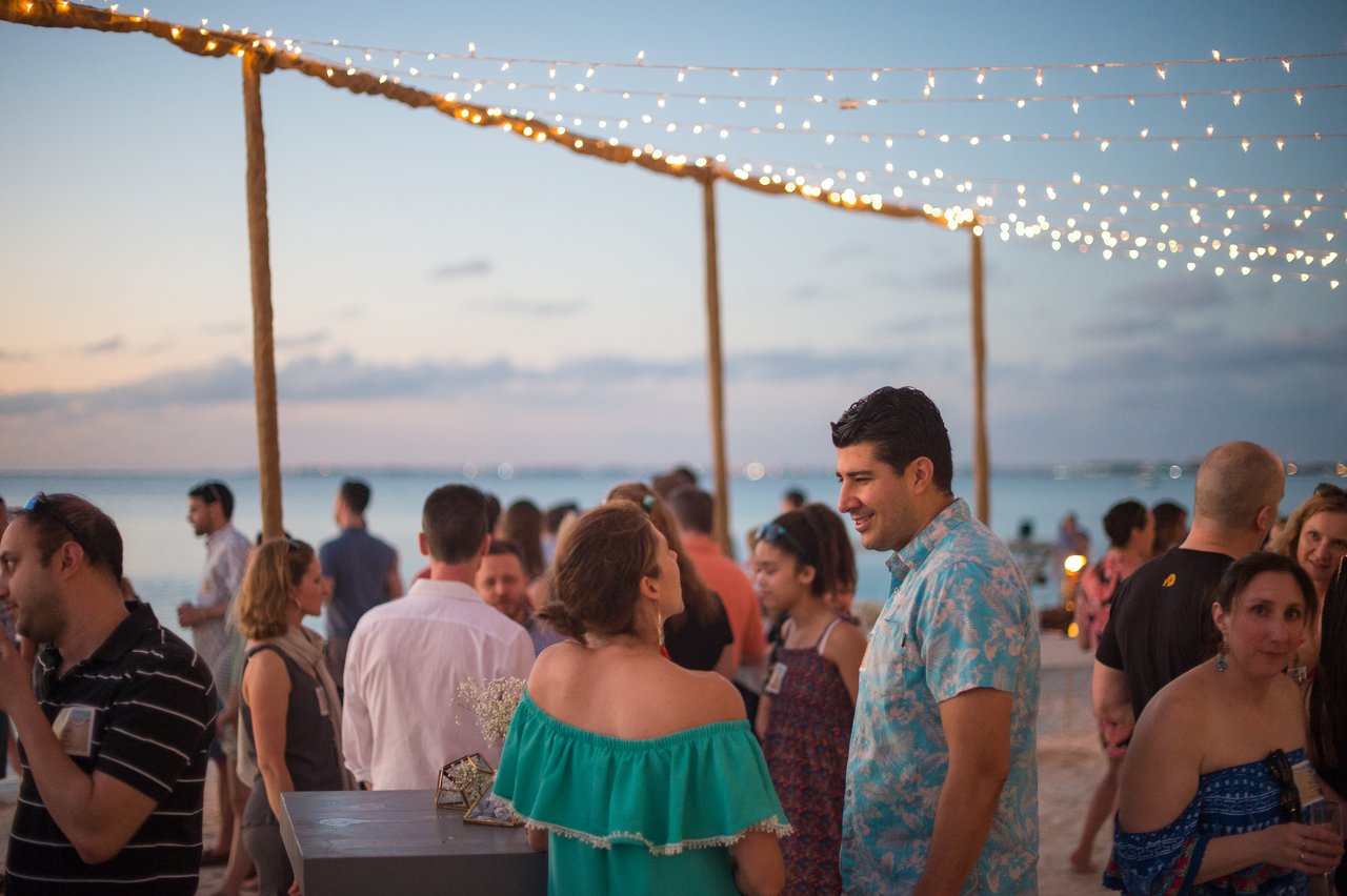 People chatting and enjoying a beach party under string lights during a company trip.