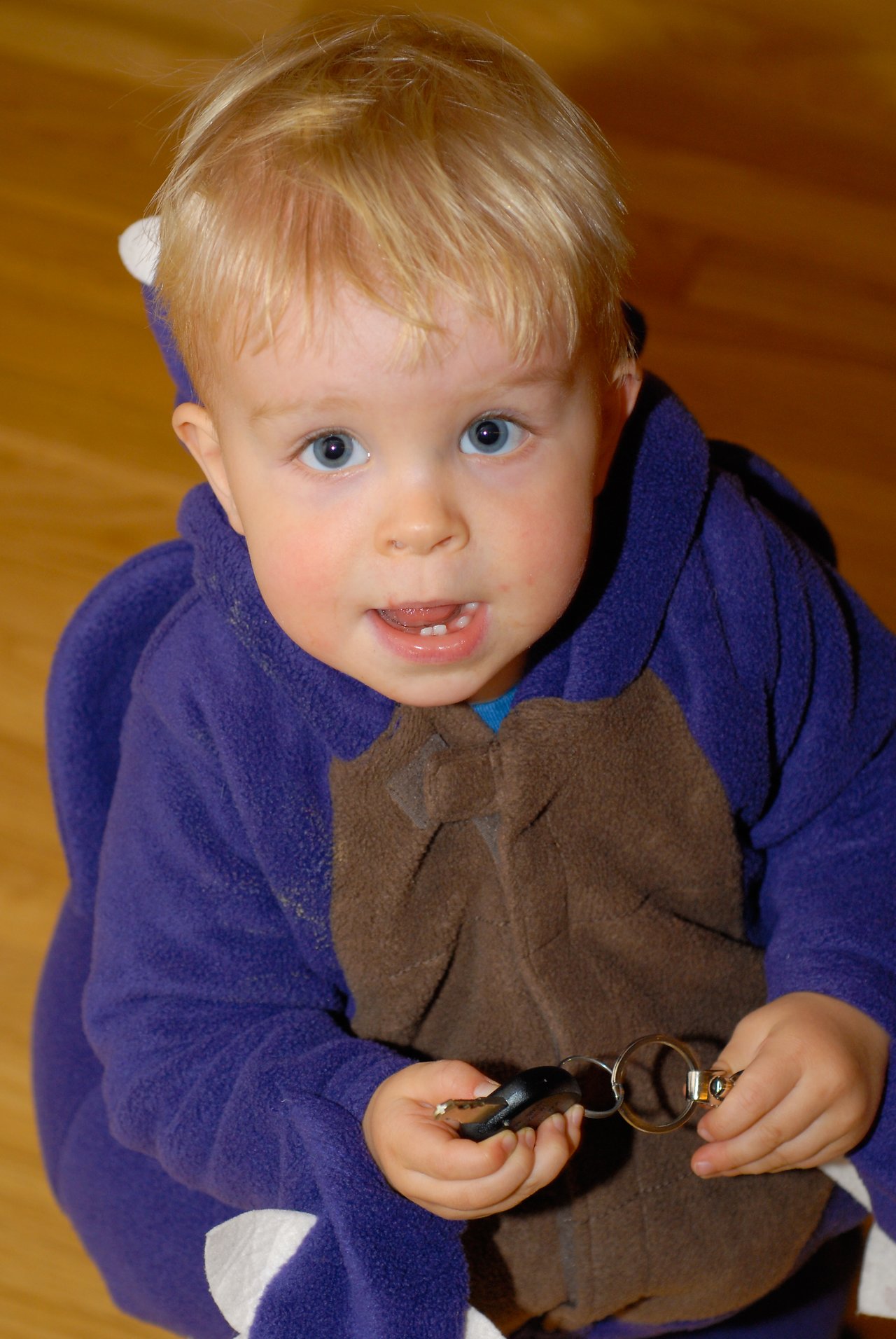 A young child in a purple and brown Halloween costume holds a set of keys while looking up.