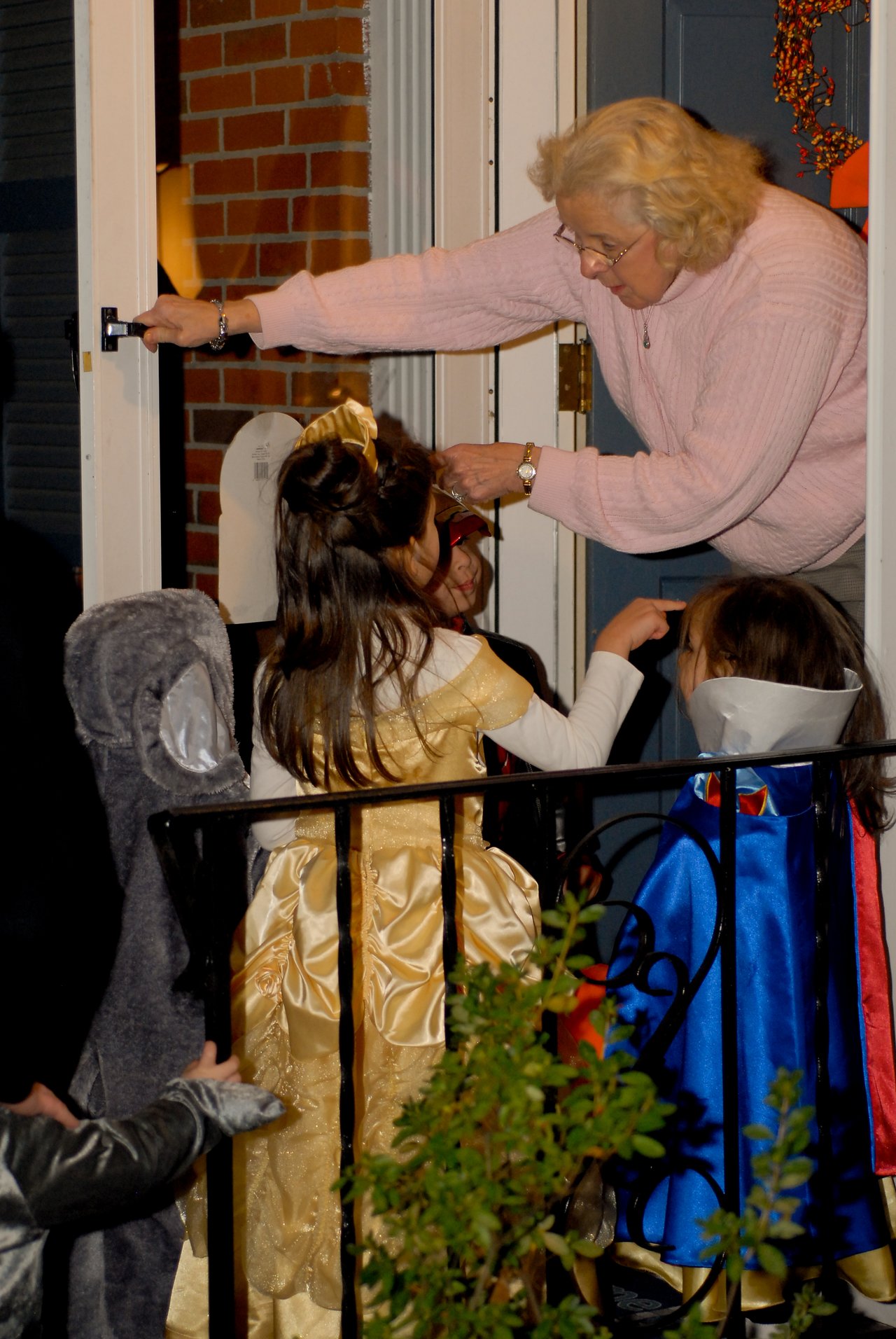 An elderly woman hands out candy to children dressed in costumes at her front door on Halloween night.