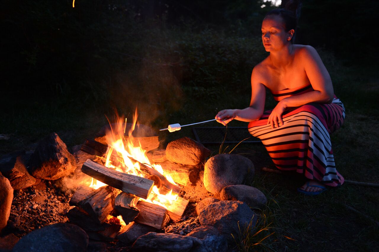 A person in a striped dress roasts a marshmallow over a campfire at night.