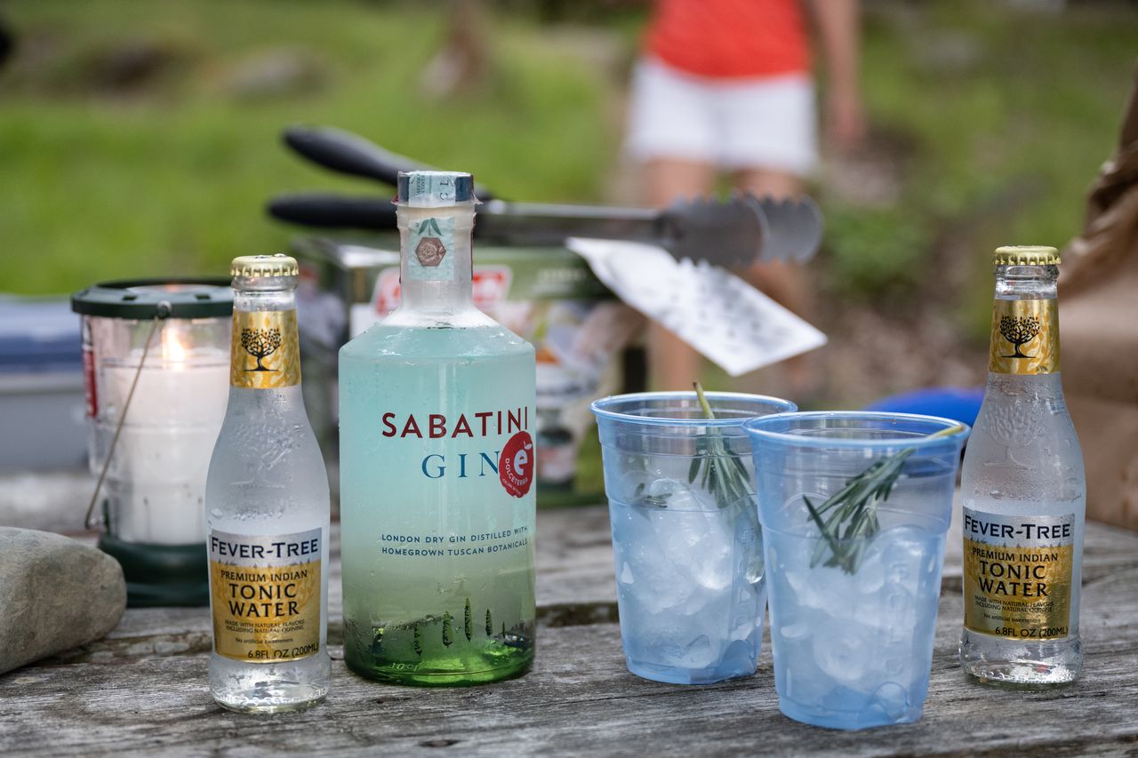 Gin and tonic drinks with ice and rosemary on a wooden picnic table during a camping trip in Maine.