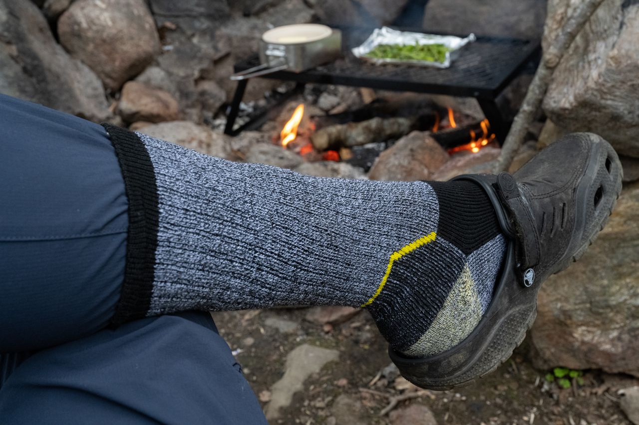A person wears thick socks with sandals near a campfire to protect against mosquitoes.