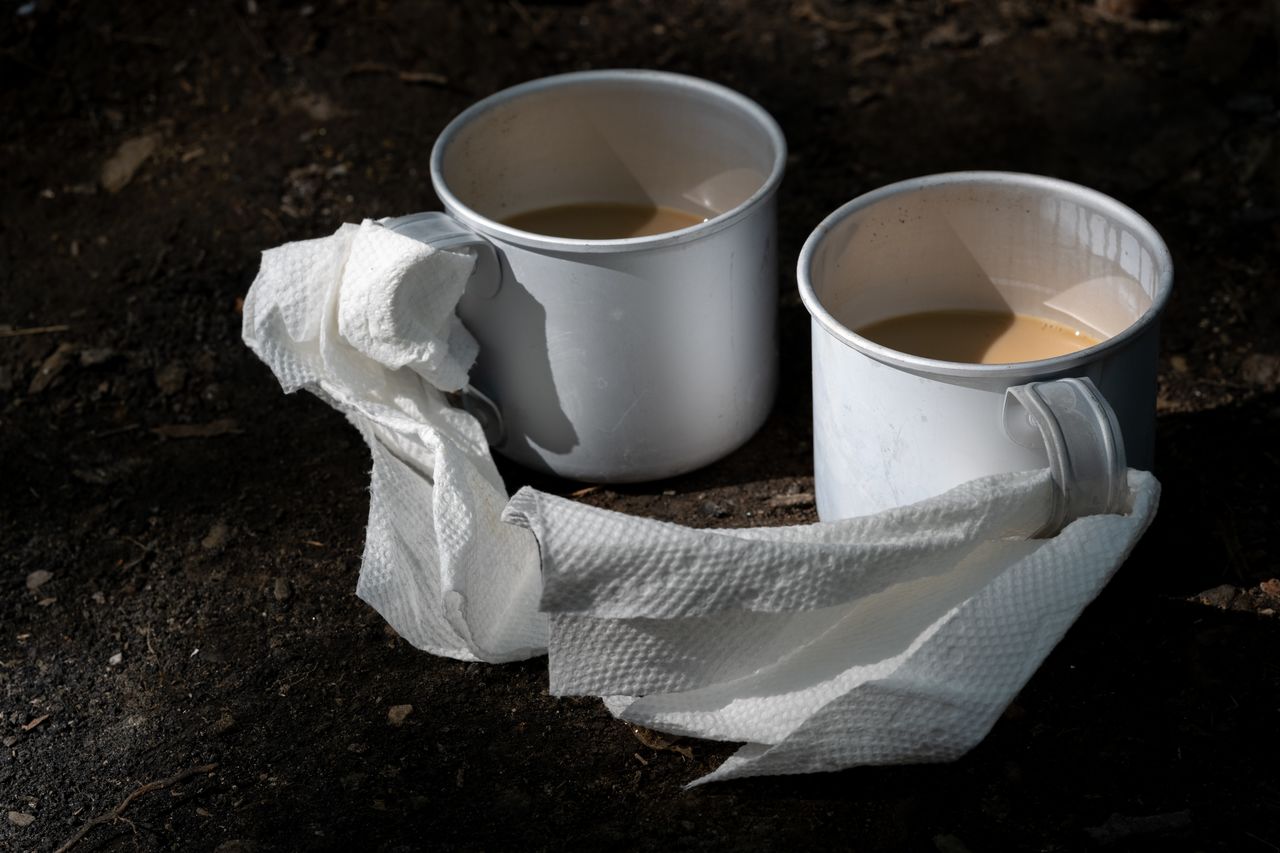 Two tin camping mugs with hot coffee and paper towels wrapped around the handles to protect from the heat.